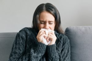 girl at home in warm knitted sweater with handkerchief, sneezes